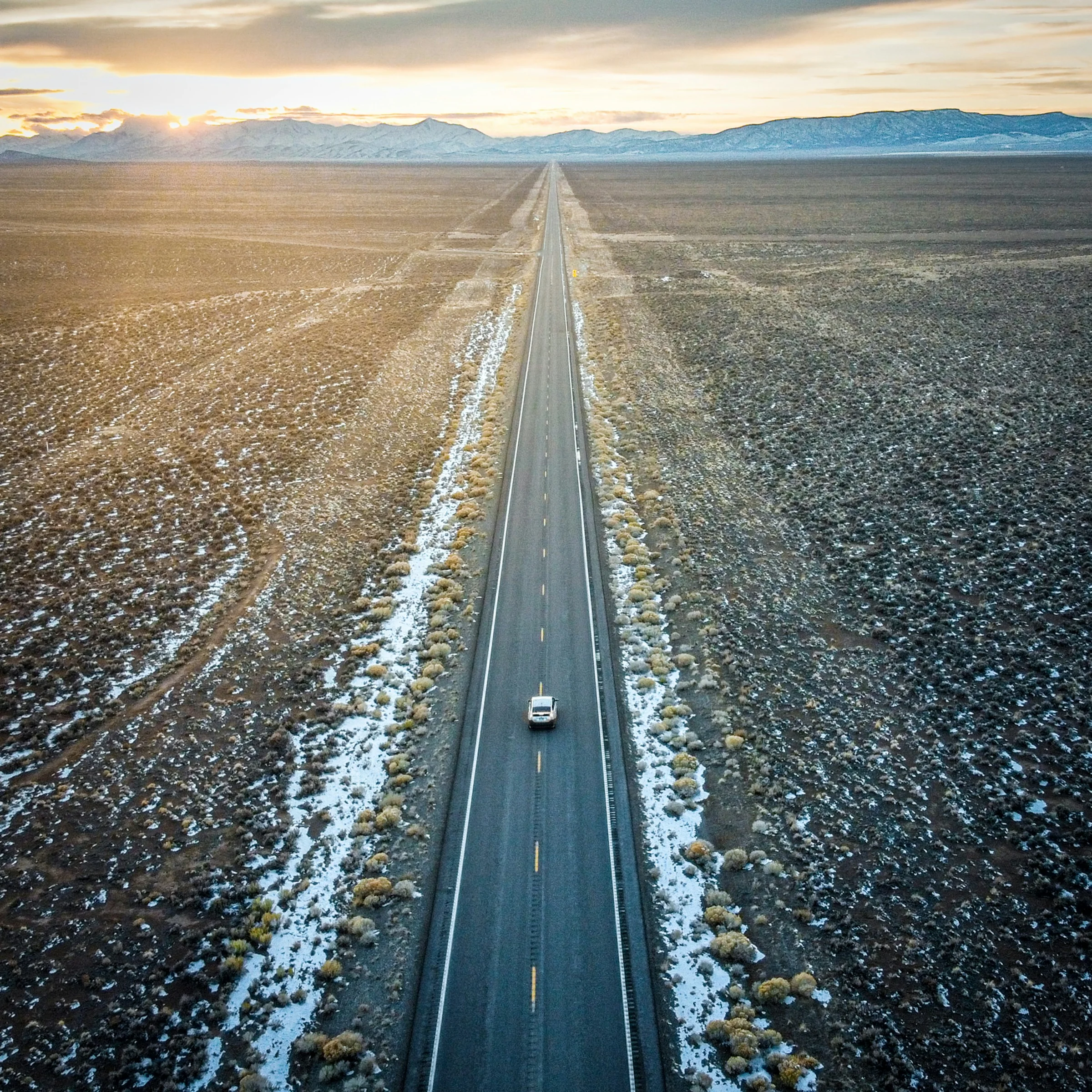 A lone car on a straight highway across the high desert at sunrise